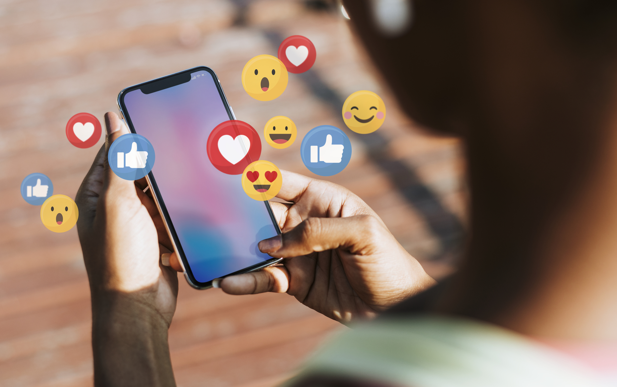 Mensch hat Smartphone in der Hand, verschiedene Smileys sind auf dem Bild neben dem Handy platziert